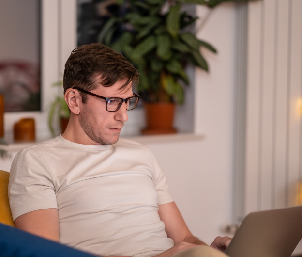 Mann mit Brille arbeitet konzentriert an einem Laptop in einem gemütlichen Raum