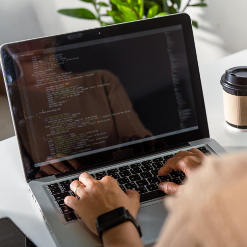 Person tippt Programmiercode auf einem Laptop mit Kaffeebecher im Hintergrund