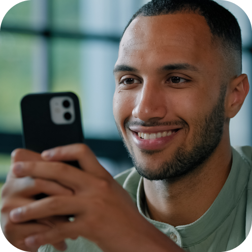 Junger Mann lächelt beim Blick auf sein Smartphone in hellem Raum