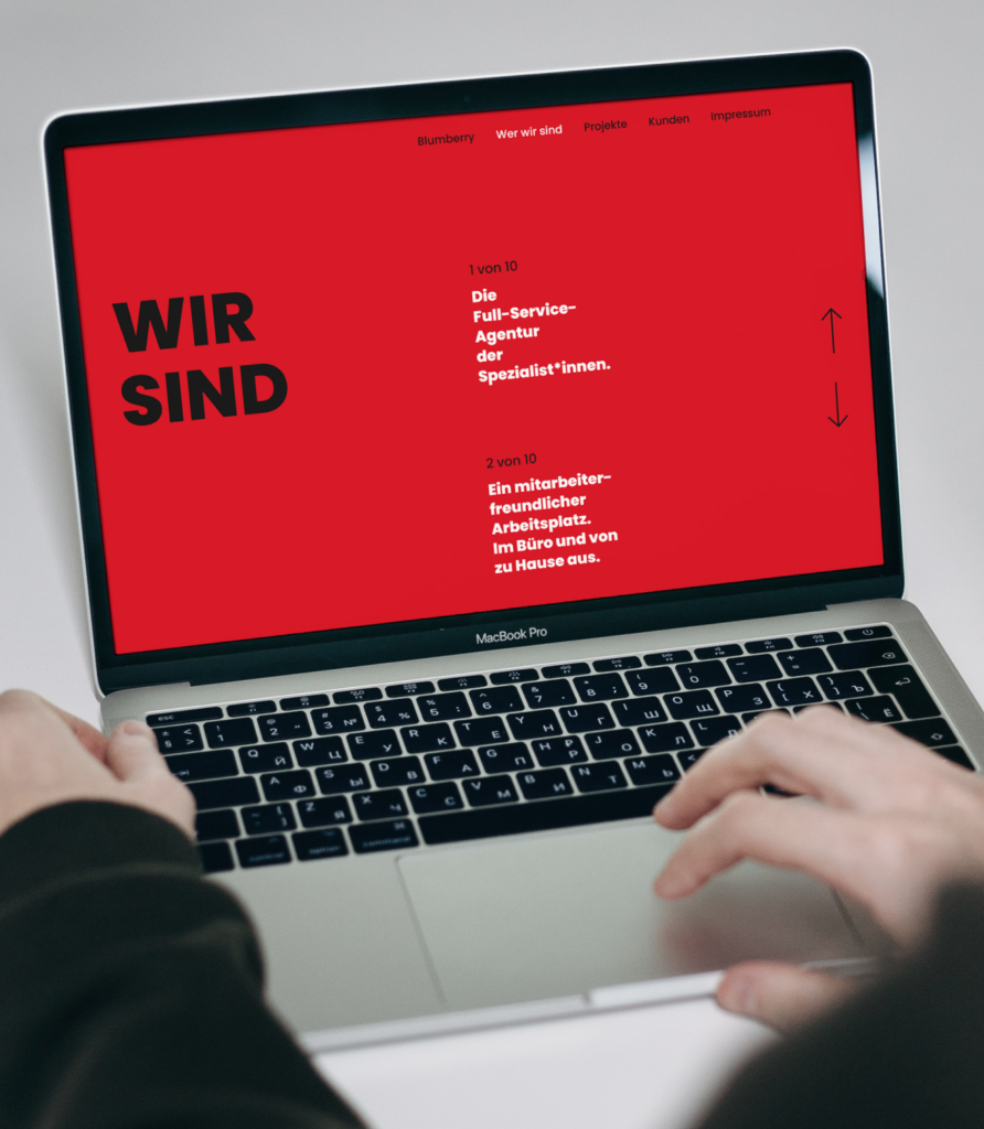 Laptop-Bildschirm zeigt rote Webseite mit dem Text "WIR SIND" und Kurzbeschreibungen einer Full-Service-Agentur.
