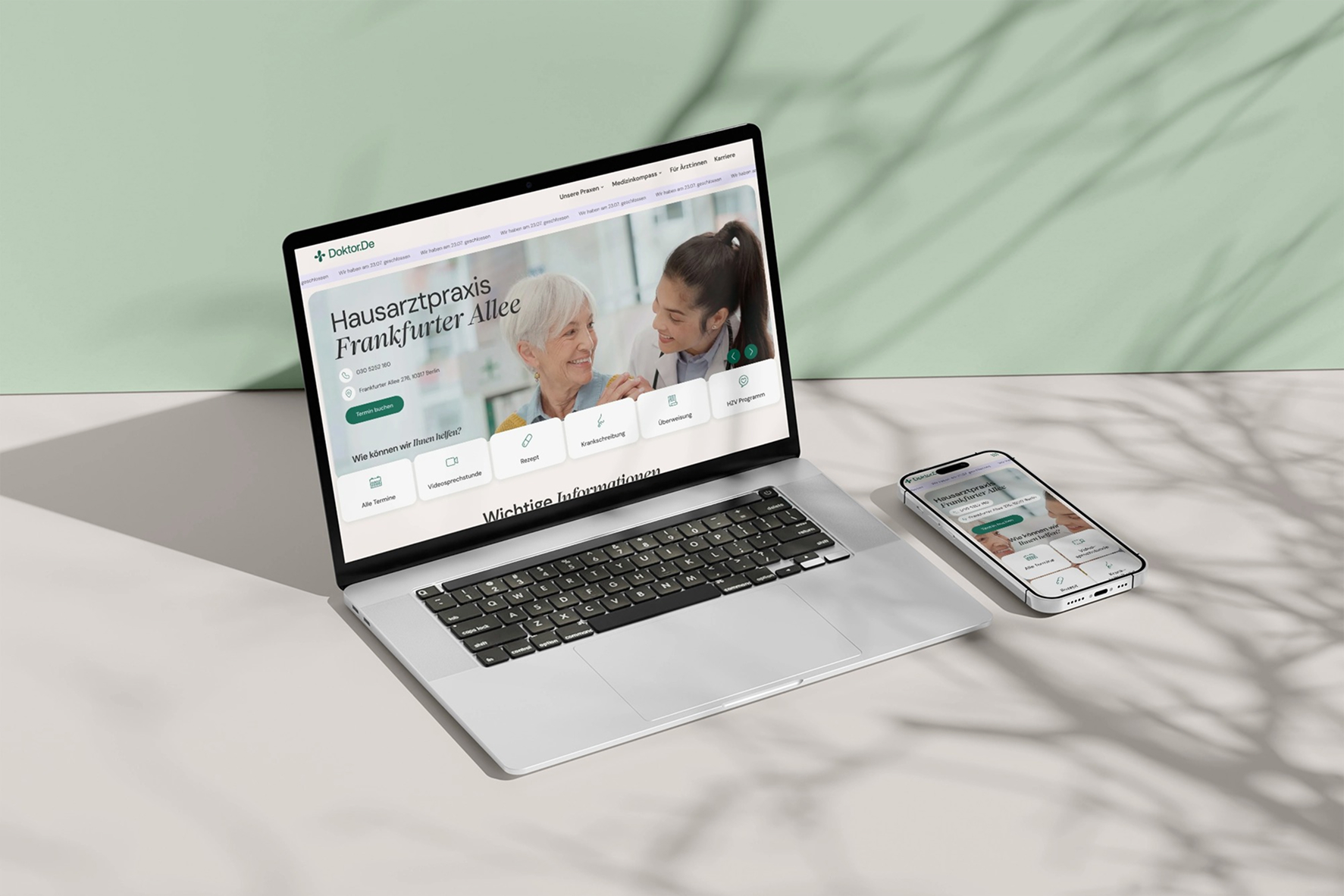 Laptop und Smartphone auf beigem Tisch, beide zeigen eine Website der Hausarztpraxis Frankfurter Allee mit Bild einer älteren Patientin und einer Ärztin, Hintergrund grün mit Baumzweigschatten
